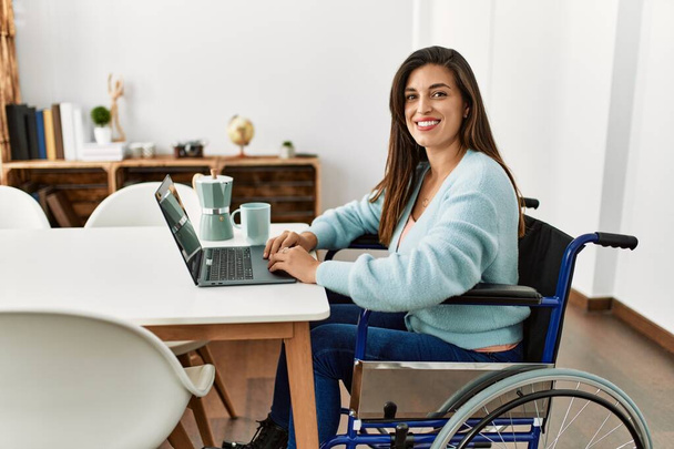 jonge vrouw met behulp van laptop zitten op rolstoel werken thuis - Foto, afbeelding