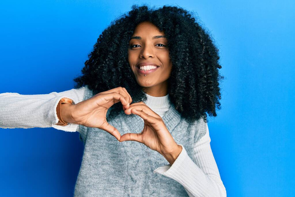 Африканская американка с афроволосами в случайном зимнем свитере улыбается в любви, делая сердце символической формы с руками. романтическая концепция.  - Фото, изображение
