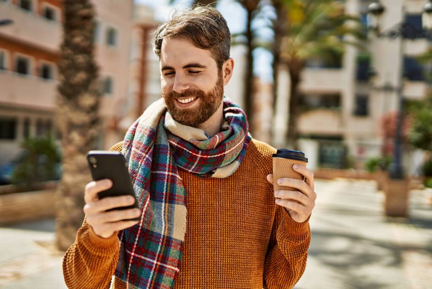 young caucasian man with beard  using smartphone outdoors on a sunny day - Foto, Imagen