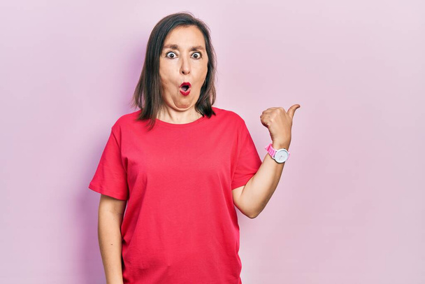 Middle age hispanic woman wearing casual clothes surprised pointing with hand finger to the side, open mouth amazed expression.  - Photo, Image