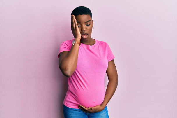 A fiatal afro-amerikai nő gyermeket vár, megérinti a terhes hasat ásít fáradt borító fél arc, szem és száj kézzel. az arc fájdalma.  - Fotó, kép