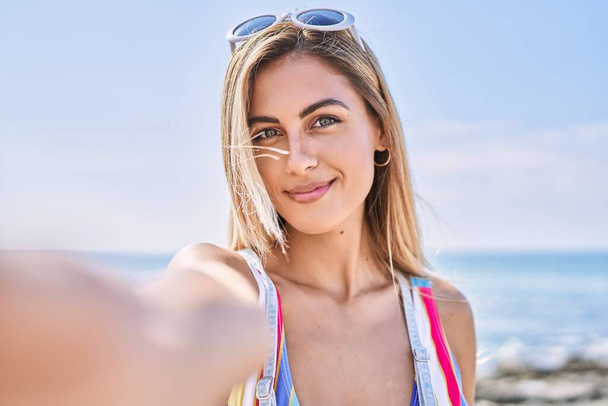 Молодая блондинка улыбается счастливая сделать селфи на смартфоне на пляже. - Фото, изображение