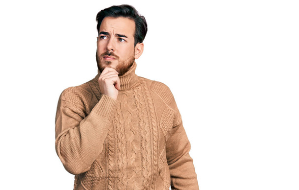 Young hispanic man wearing casual clothes with hand on chin thinking about question, pensive expression. smiling with thoughtful face. doubt concept.  - Photo, Image