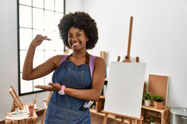 Joven mujer afroamericana con el pelo afro en el estudio de arte gesto con las manos mostrando signo de tamaño grande y grande, medir símbolo. sonriendo mirando a la cámara. concepto de medición.  - Foto, imagen