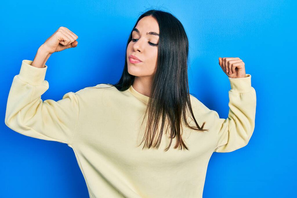 Young brunette woman wearing casual sweatshirt showing arms muscles smiling proud. fitness concept.  - Foto, Imagen