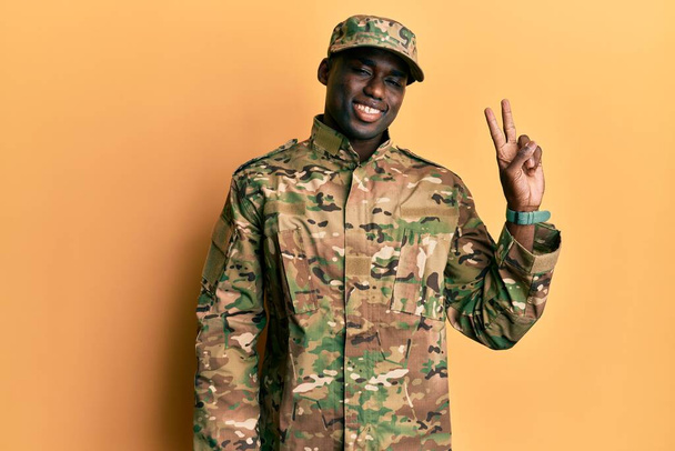 軍の制服を着た若いアフリカ系アメリカ人男性が笑顔でカメラに向かってウィンクし、指で勝利サインをしています。2番.  - 写真・画像