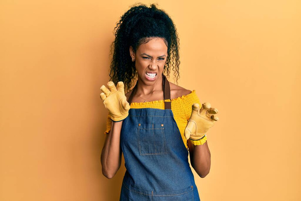 Middle age african american woman wearing professional apron smiling funny doing claw gesture as cat, aggressive and sexy expression  - Fotografie, Obrázek