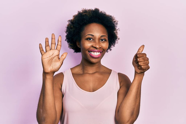 Jovem afro-americana vestindo camiseta casual sem mangas mostrando e apontando para cima com os dedos número seis enquanto sorri confiante e feliz.  - Foto, Imagem