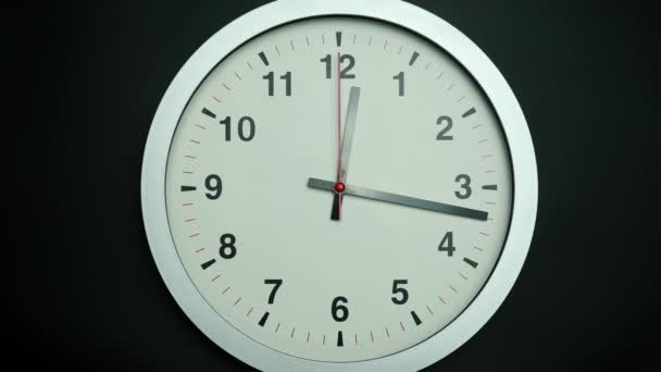 L'orologio da parete bianco indica l'ora lentamente. Lenta rotazione dell'orologio su terra nera. - Filmati, video