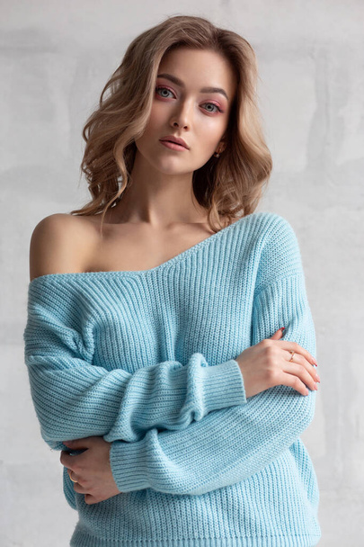 Sexy blonde girl in a blue knitted sweater on a white wall background. Fashion photo of a gorgeous close-up model - Valokuva, kuva