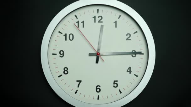 Weiße Wanduhr zeigt die Mittagszeit und 15 Minuten an. Die Zeit vergeht langsam an einem Tag auf schwarzem Hintergrund. - Filmmaterial, Video