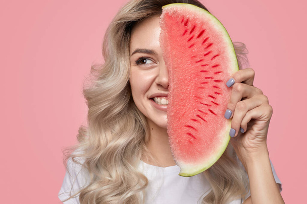 Smiling young woman smiling while holding watermelon slice near face in studio - Foto, Imagem