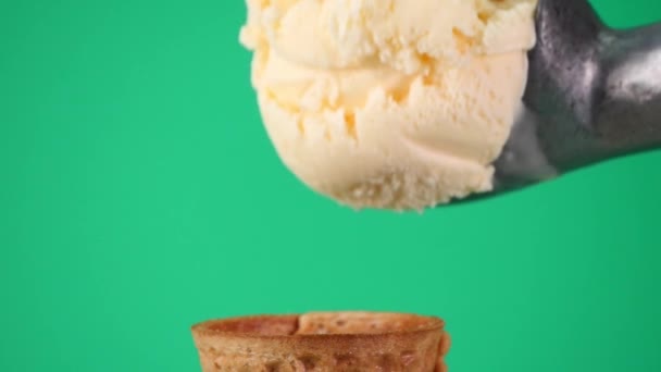 Schep Vanille ijs met lepel op wafelkegel. Textuur van het zachte ijs op de kegel. over groene achtergrond. - Video
