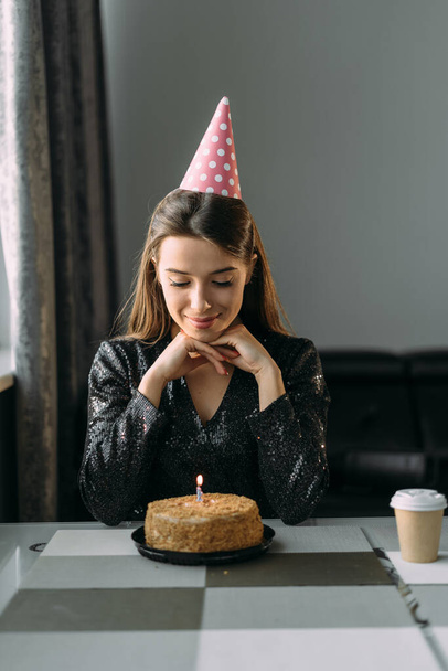 Onnellinen nuori nainen kynttilän kanssa syntymäpäiväkakussa kotona. Lähikuva herkullinen kakku pöydälle, kun nainen tekee syntymäpäivätoiveen. Iloinen tyttö juhlii 25-vuotissyntymäpäiväänsä yksin kotona - Valokuva, kuva