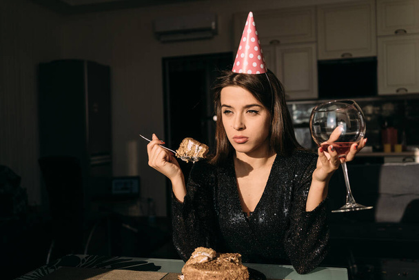 triste fiesta de cumpleaños en casa, mujer joven comiendo pastel y bebiendo vino, celebrando aniversario solo, 25 años de fiesta, espacio para el texto - Foto, Imagen