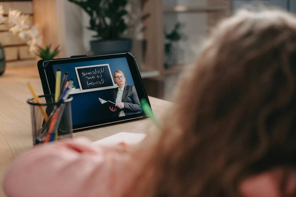Rückansicht eines Schulmädchens, das mit einem Lehrer im virtuellen Klassenzimmer per digitalem Tablet spricht. Schreibtest Mathe. Moderne Online-Bildung. Entfernung - Foto, Bild