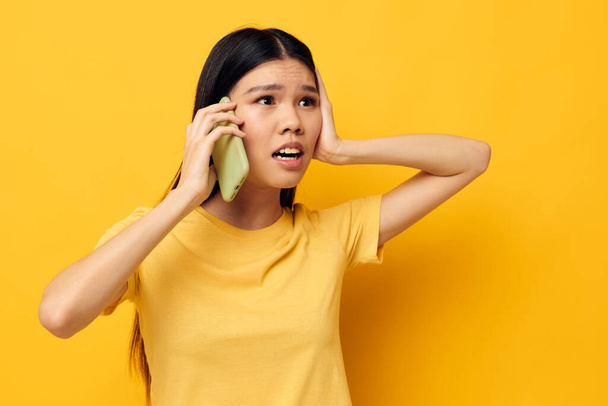 Charming young Asian woman communicates on the phone emotions yellow background unaltered - Photo, Image