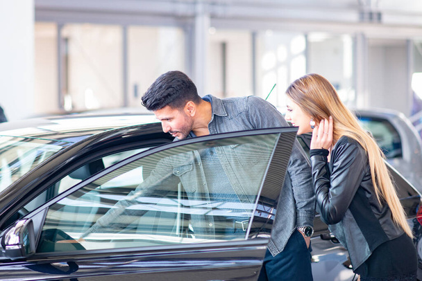 Young couple choosing new car for buying in dealership shop - Foto, immagini
