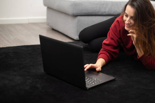 Young woman using a laptop while relaxing in her apartment - Foto, Imagen