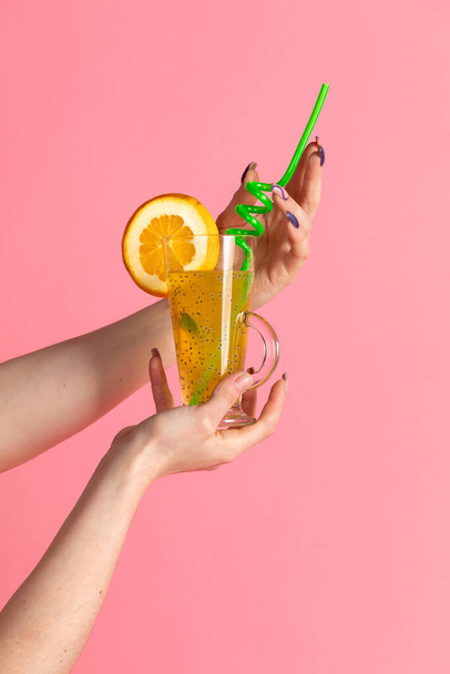 A glass with a fruit cocktail on a pink background. Womens hands hold a drink - Fotografie, Obrázek