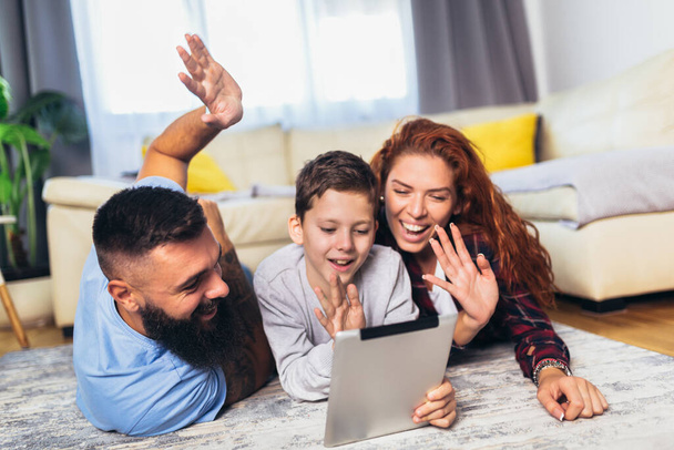 Famille heureuse avec un enfant couché sur le tapis et utilisant une tablette numérique
 - Photo, image