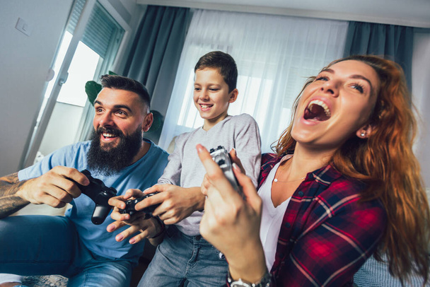 Ευτυχισμένη οικογένεια που παίζει βιντεοπαιχνίδια στο σπίτι και διασκεδάζει μαζί. - Φωτογραφία, εικόνα