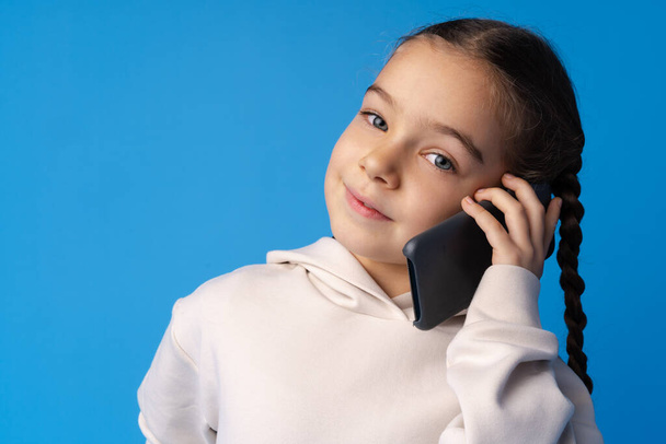 Маленька дівчинка розмовляє по телефону на синьому фоні
 - Фото, зображення