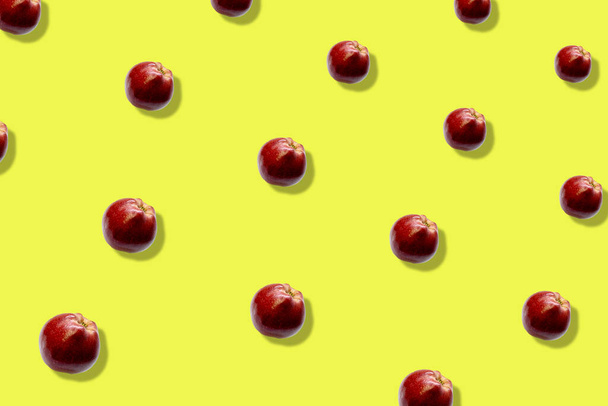 Colorful fruit pattern of fresh red apples on yellow background. Top view. Flat lay. Pop art design, creative summer concept - 写真・画像