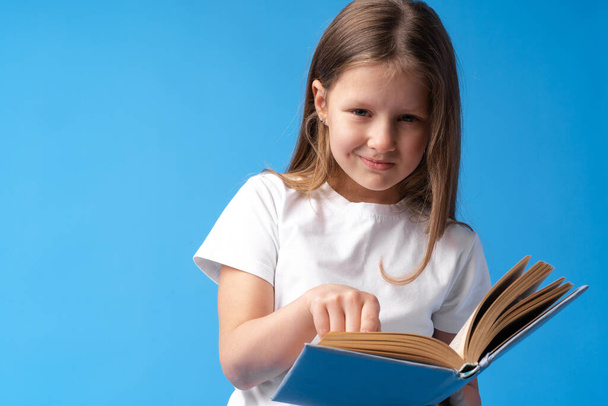 Little beautiful smiling girl holding book against blue background - Foto, immagini