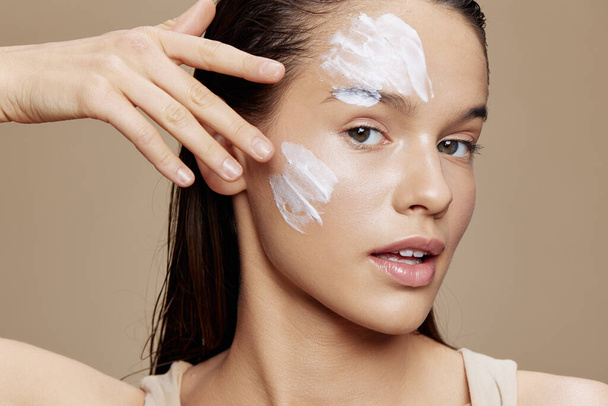 brunetta cura della pelle utilizzando maschera bianca sul viso sfondo beige - Foto, immagini