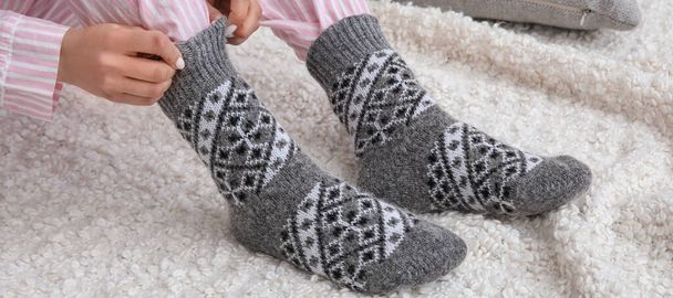 Woman putting on her warm knitted socks at home. Concept of heating season - Photo, Image