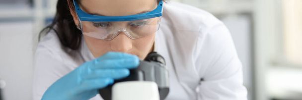 Jeune femme scientifique avec des lunettes regarde à travers le microscope gros plan - Photo, image