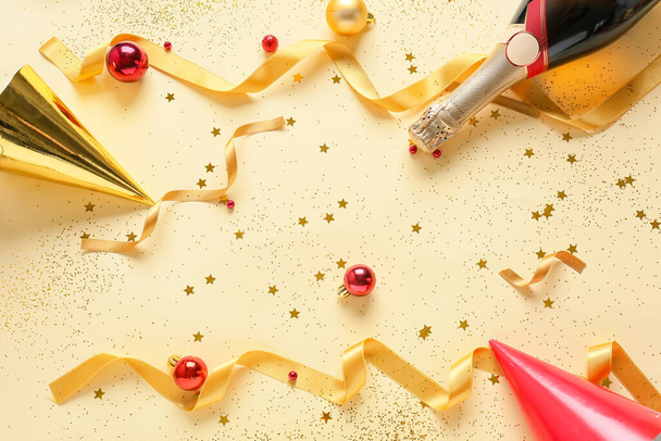 Golden ribbons with Christmas balls, bottle of champagne, confetti and party hats on light background - Photo, Image