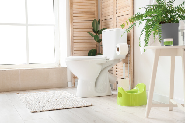 Innenraum der hellen Toilette mit grünem Töpfchen, Halter mit Papierrollen und Toilettenschüssel - Foto, Bild