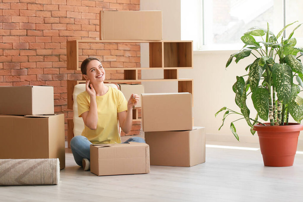 Mujer joven y feliz con llave y cajas sentadas en el suelo en su nuevo apartamento - Foto, Imagen