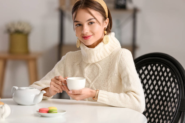 Όμορφη νεαρή γυναίκα πίνοντας νόστιμο τσάι στο τραπέζι στο καφέ - Φωτογραφία, εικόνα