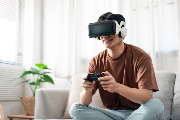 Technology Concept A person wearing a virtual reality headset and holding a black console game while sitting on the sofa. - Photo, Image