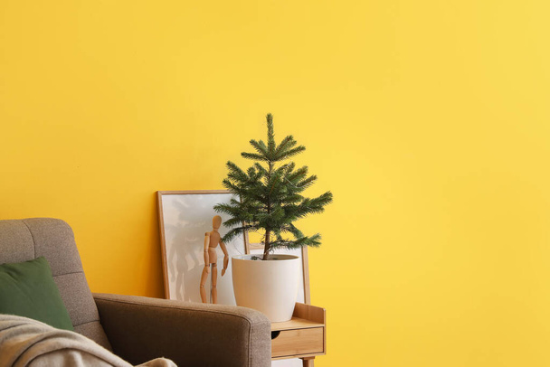 Pequeño árbol de Navidad en maceta en la mesa cerca de la pared de color en la habitación - Foto, Imagen