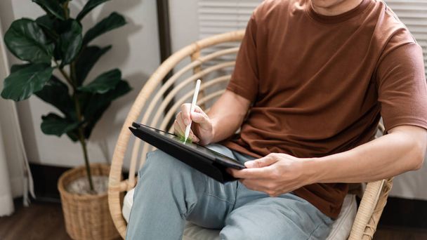 Концепция технологии Молодой человек, который сидит на стуле, держа свой iPad и отмечая что-то на нем. - Фото, изображение