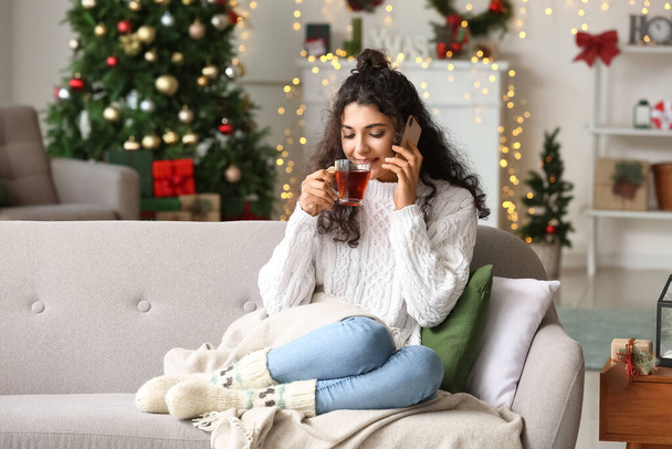 Bella donna che beve tè e parla per telefono a casa la vigilia di Natale - Foto, immagini