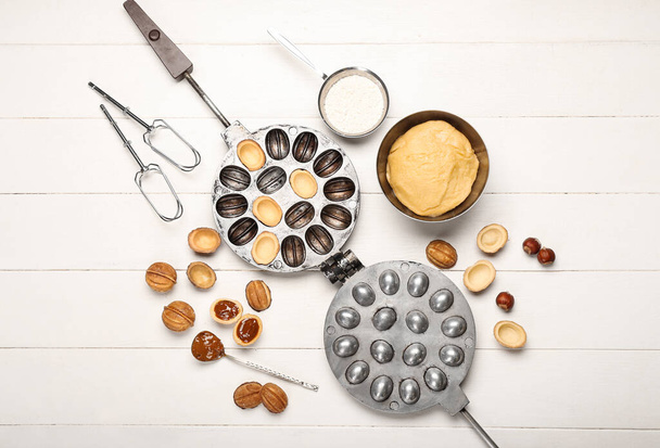 Schaal van vers deeg en ingrediënten voor het bereiden van smakelijke walnoot vormige koekjes met gekookte gecondenseerde melk op witte houten achtergrond - Foto, afbeelding
