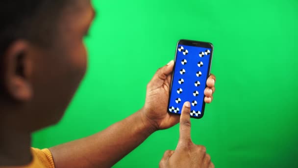 アフリカ系アメリカ人男性は緑の背景に追跡マーカーとスマートフォンでオンラインストアをスクロールします - 映像、動画