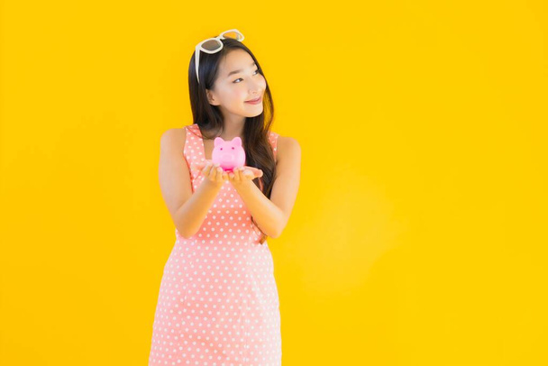 Ritratto bella giovane donna asiatica mostrano un sacco di soldi o contanti con salvadanaio su sfondo giallo isolato
 - Foto, immagini