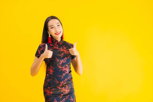 Portret mooie jonge aziatische vrouw dragen Chinese jurk met actie voor Chinese nieuwjaar concept op gele geïsoleerde achtergrond - Foto, afbeelding