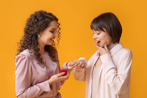 Young lesbian woman proposing to her girlfriend on color background - Photo, Image