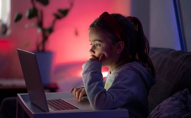 A little girl uses a laptop late at night. - Фото, изображение