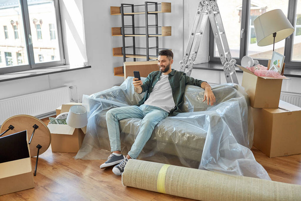 man with smartphone and boxes moving into new home - Foto, Bild