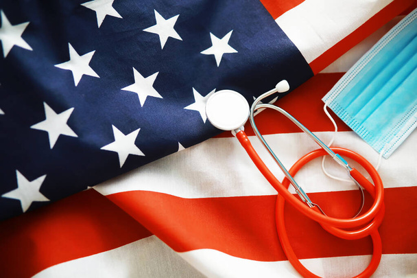 Amerikkalainen terveydenhuoltojärjestelmä. USA:n lipun tausta. Lääketieteellinen naamio ja stetoskooppi. - Valokuva, kuva
