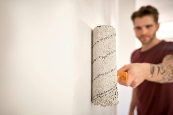 Hombre caucásico pintando pared en casa nueva con un rodillo de pintura - Foto, Imagen
