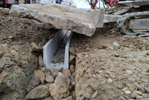 A escavadeira instala bandejas de concreto para drenagem de águas pluviais em áreas rurais, produtos de concreto para drenagem de água. - Foto, Imagem